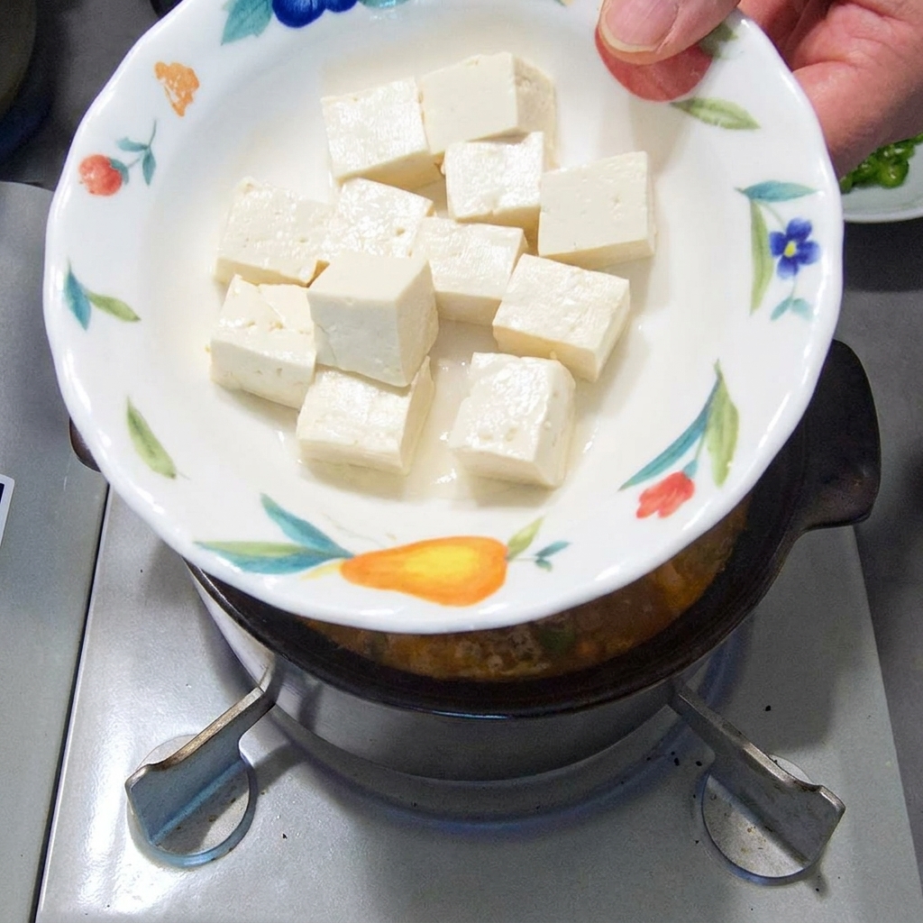 Cubetti di tofu bianco morbido aggiunti nello stufato in ebollizione.