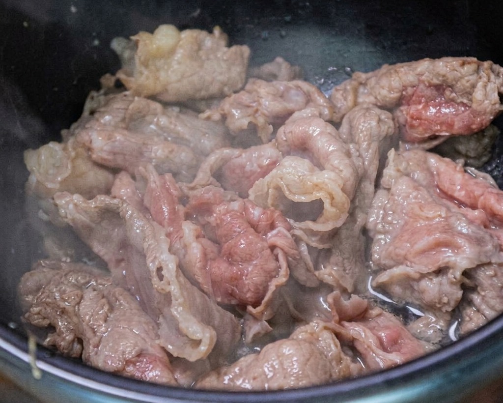 Manzo che viene saltato in padella con aglio tritato e cipollotti freschi.