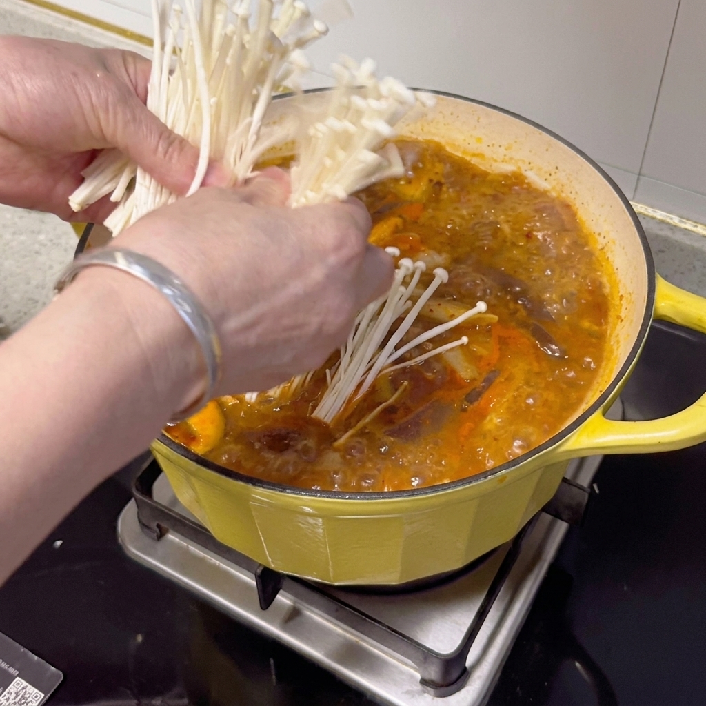 Funghi enoki freschi, cipollotti e fette di peperoncino disposti sopra lo stufato finito.