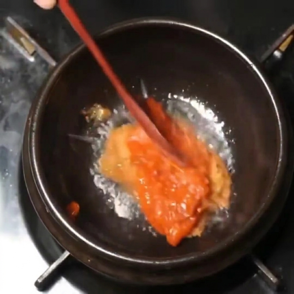 Miscela densa di salse rosse e marroni mescolata con un cucchiaio di legno in una pentola nera a fuoco basso.