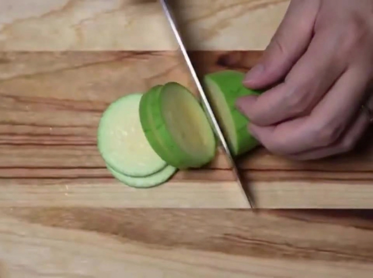 Una zucchina verde tagliata in mezzelune uniformi su un tagliere di legno.