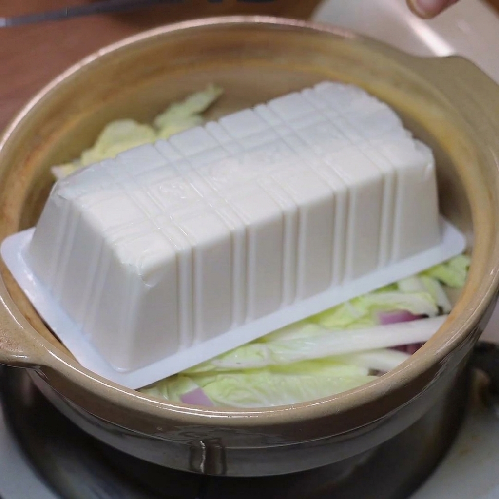 Fette di tofu morbido disposte sopra il cavolo e le cipolle nella pentola di terracotta.
