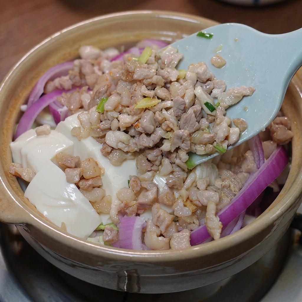 Il maiale saltato e la salsa preparata versati sopra il tofu nella pentola di terracotta.