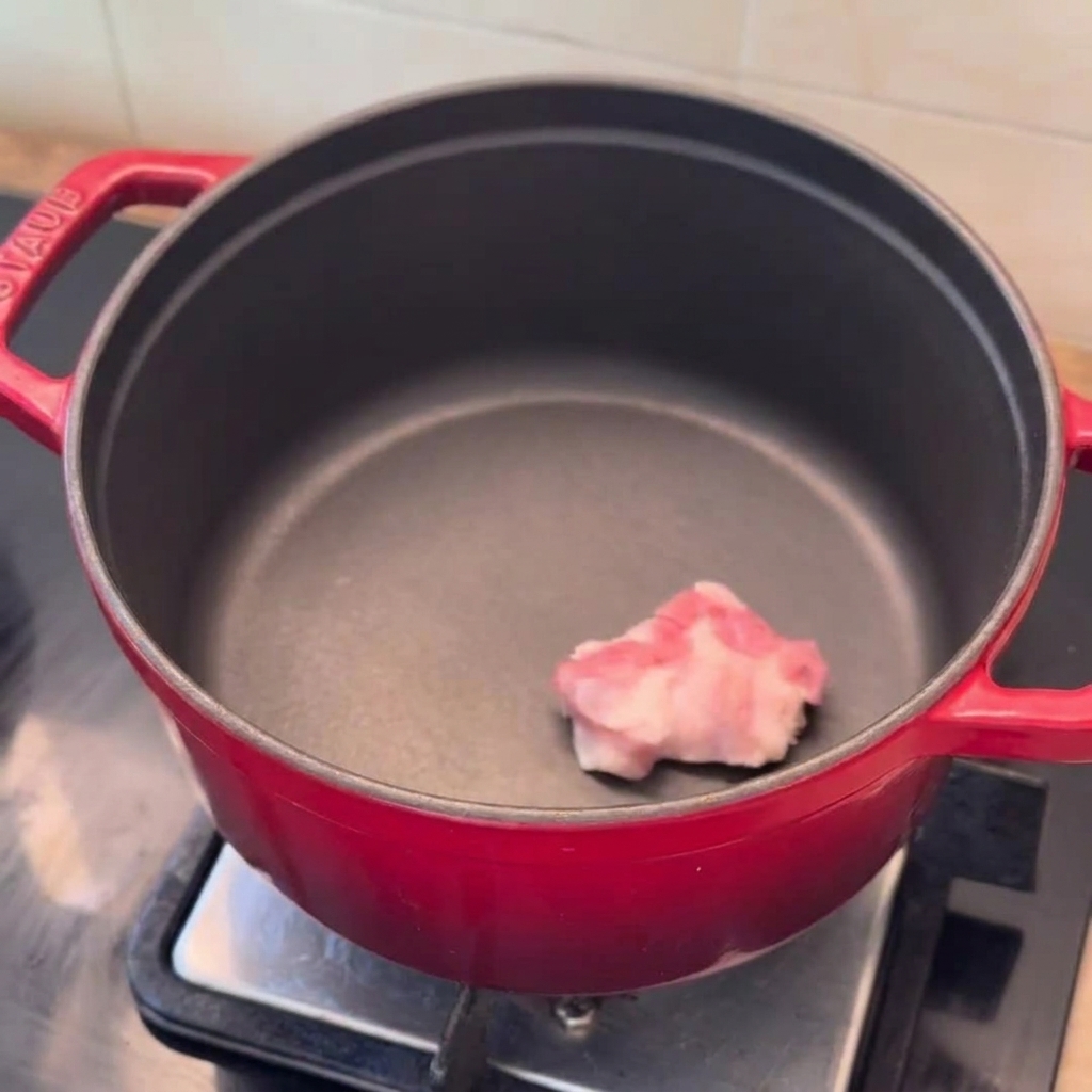 Fette di pancetta, spicchi di cipolla e aglio tritato pronti in una pentola rossa preriscaldata.