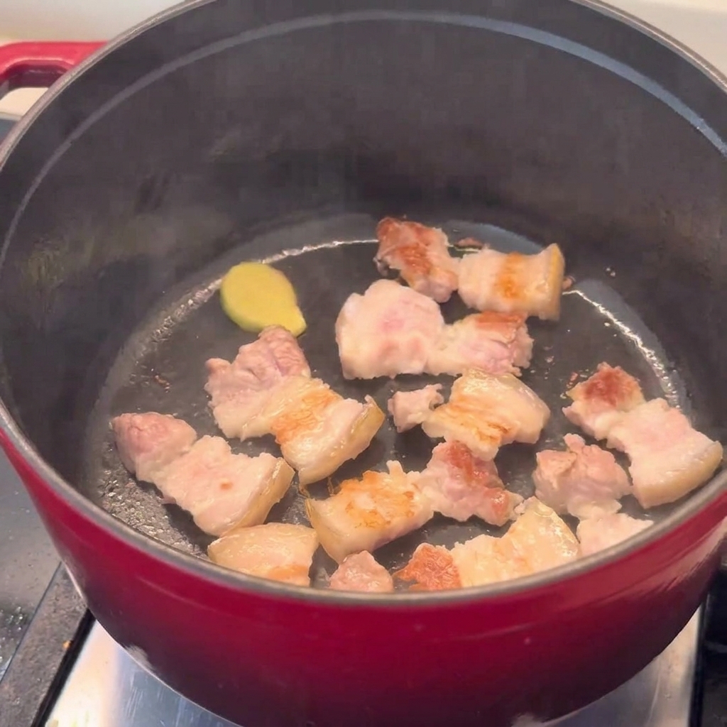 Pezzi di pancetta dorati che soffriggono in una pentola rossa.