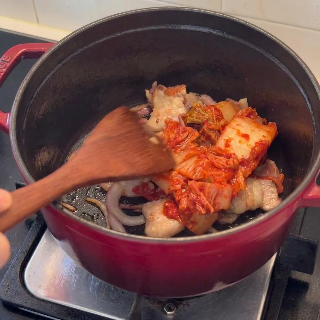 Pezzi di kimchi che vengono saltati insieme alla pancetta rosolata in una pentola.