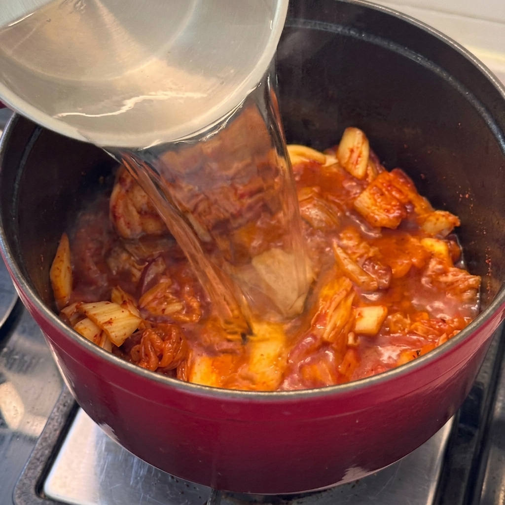 Acqua versata nella pentola con il mix di maiale e kimchi per iniziare la base dello stufato.
