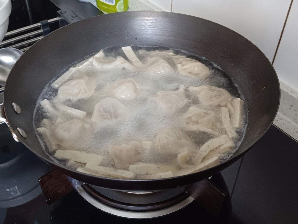 Primo piano di vermicelli immersi nella pentola con ravioli e tofu.