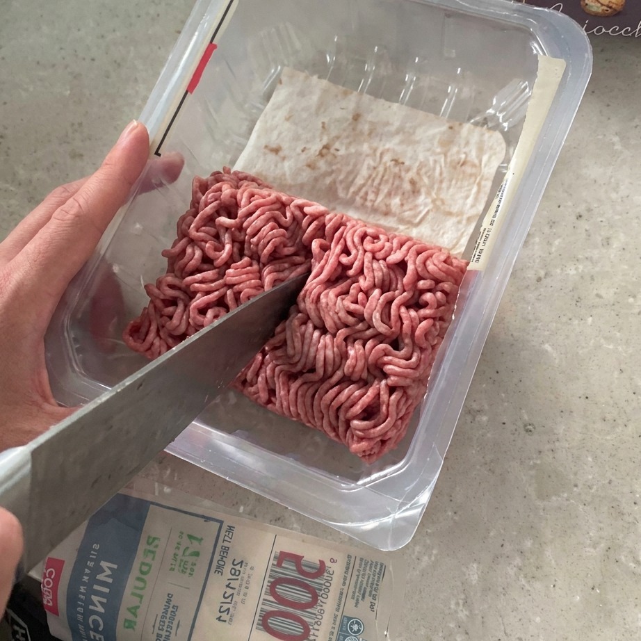 Macinato di manzo tagliato a metà con un grosso coltello allinterno della sua confezione.