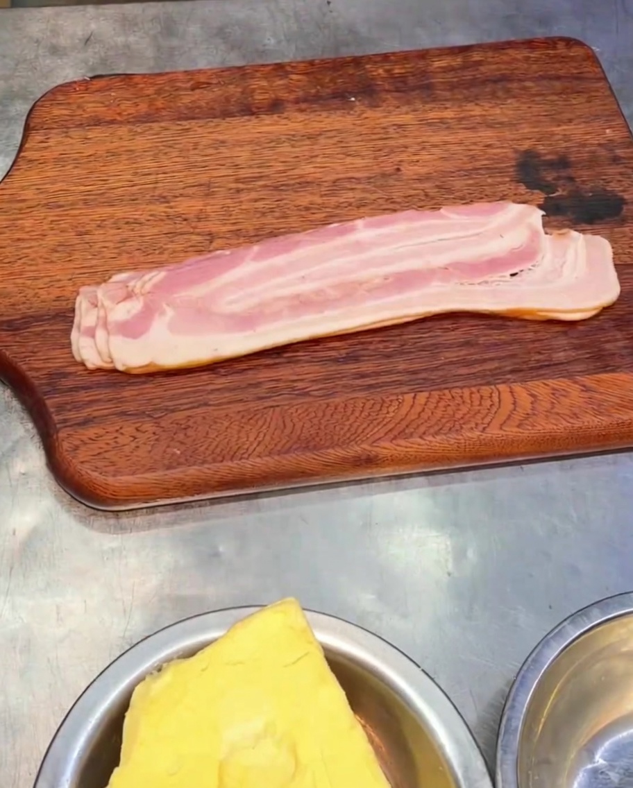 Pezzi di bacon affumicato affettato su un tagliere di legno.