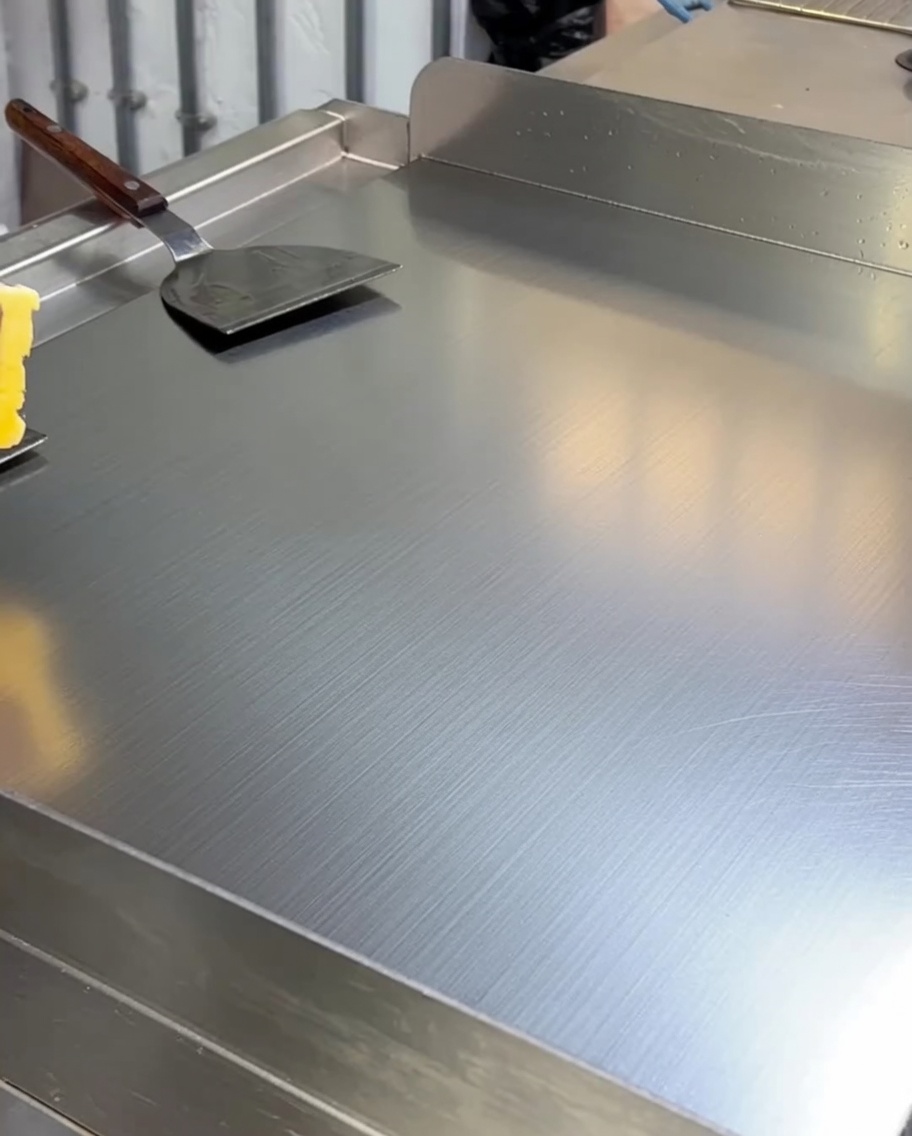 Burro giallo che si scioglie e riveste la superficie di una piastra calda in acciaio inox.
