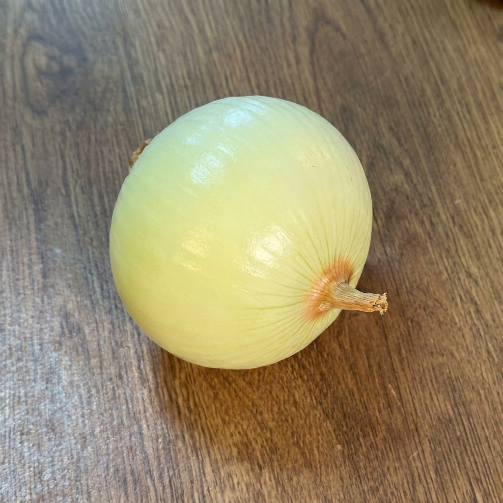 Una cipolla intera sbucciata su un piano di legno.
