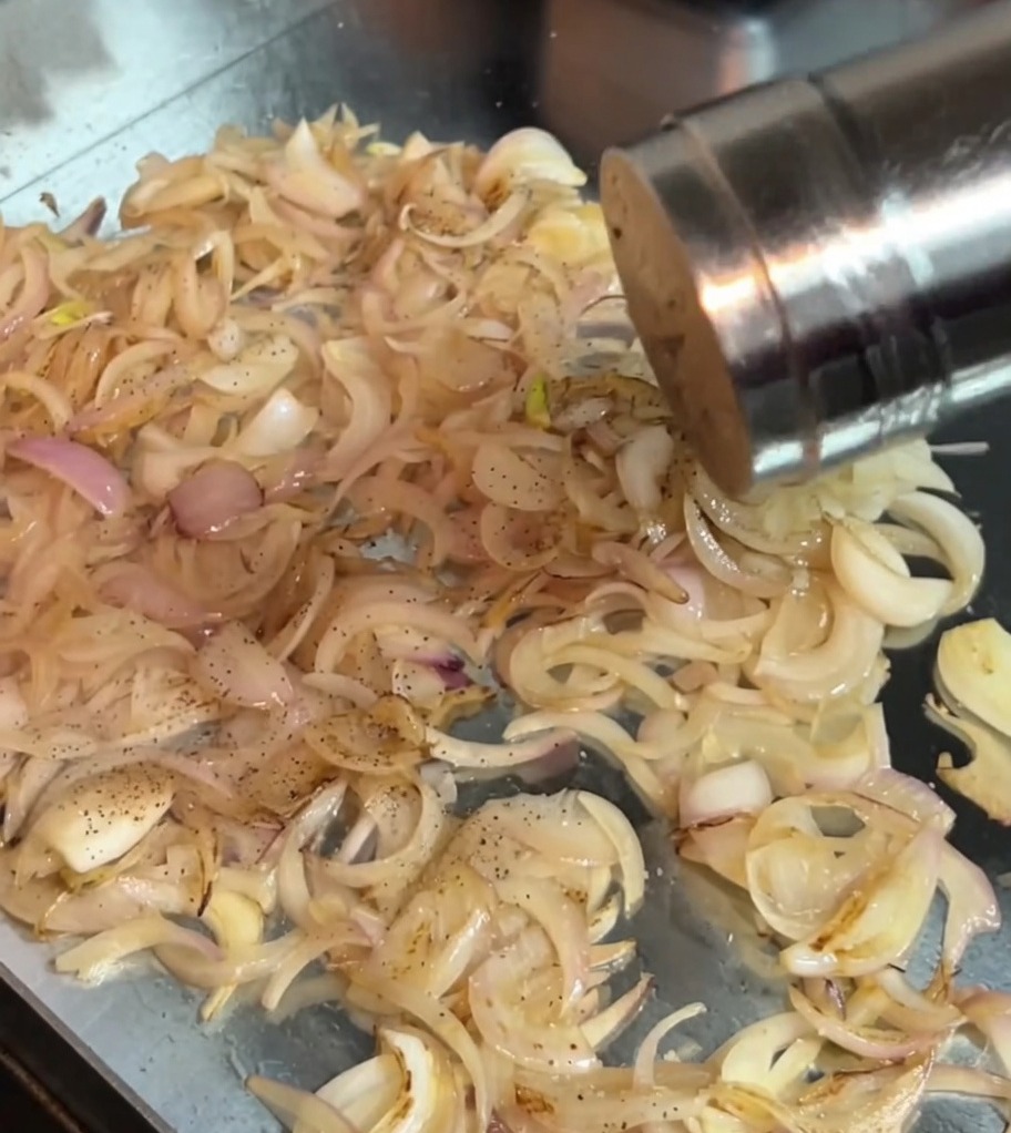 Sale e pepe nero cosparsi sulle cipolle saltate in padella.