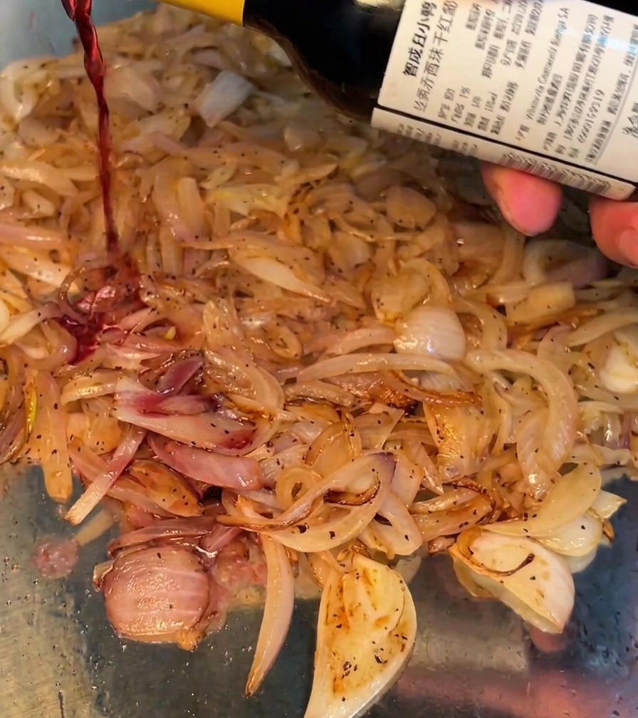 Vino rosso versato nella padella con le cipolle che soffriggono.