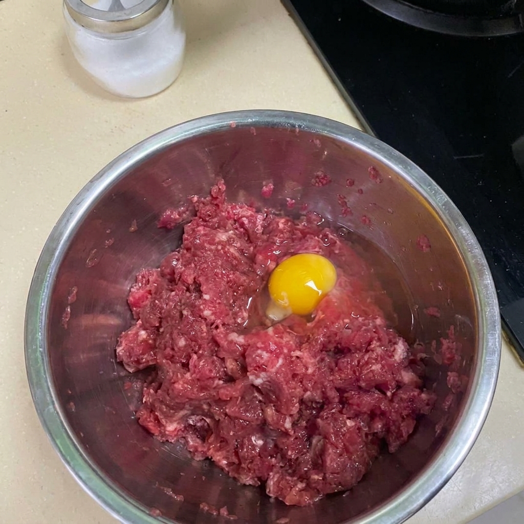 Carne macinata mescolata con spezie e uovo in una ciotola di metallo.