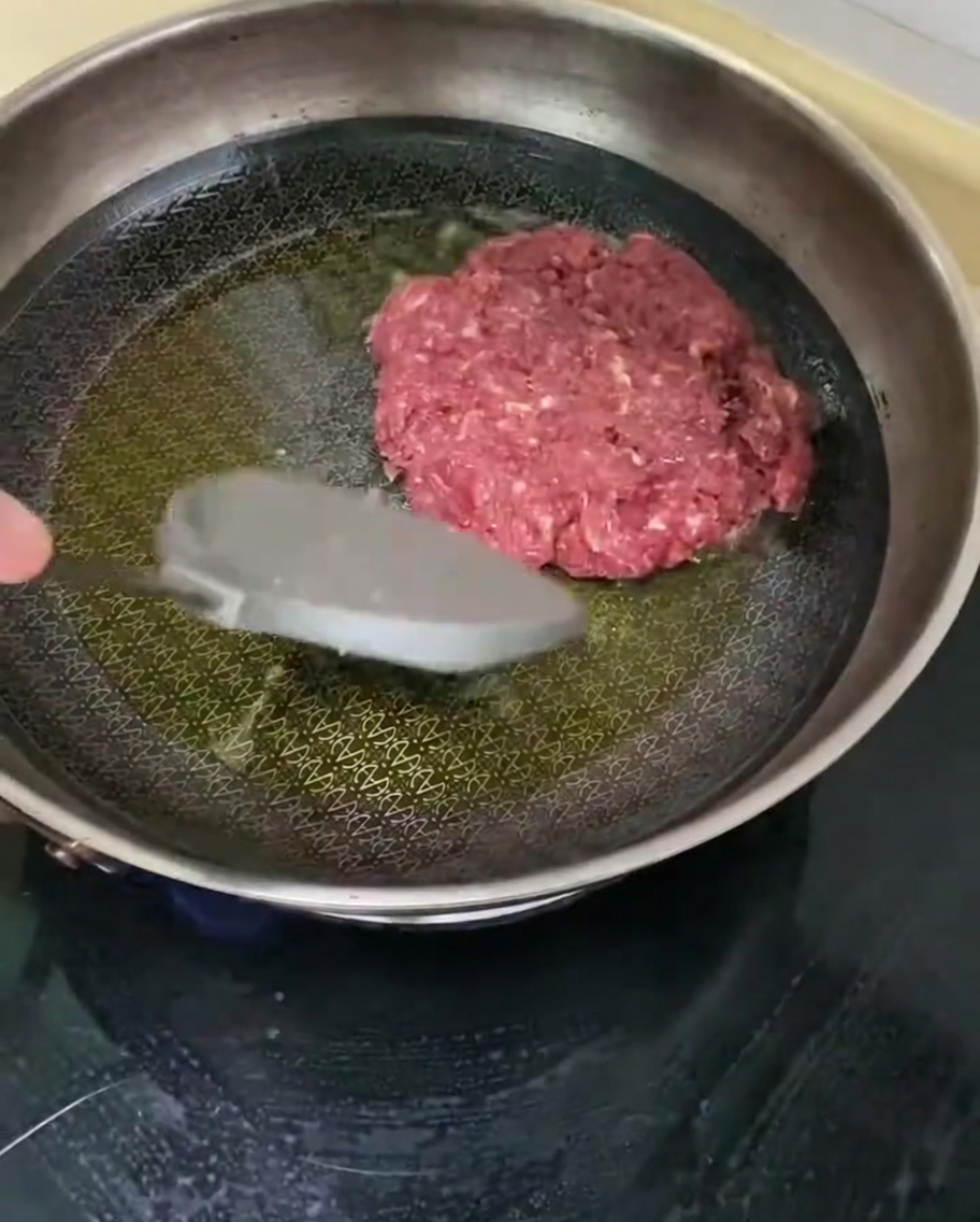 Un hamburger di manzo che frigge in una padella calda.