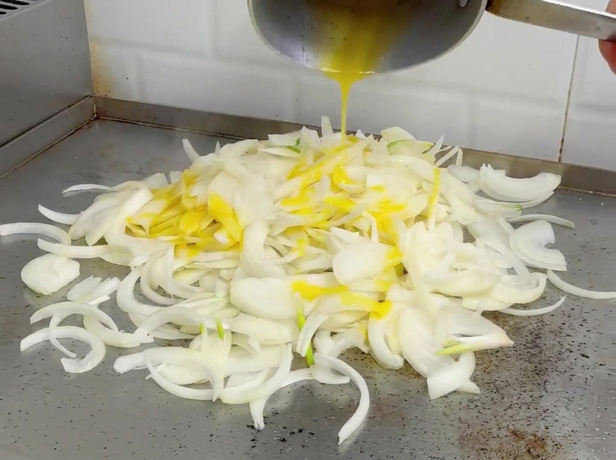 Cipolle saltate su una piastra calda, dallaspetto ammorbidito e leggermente dorato.