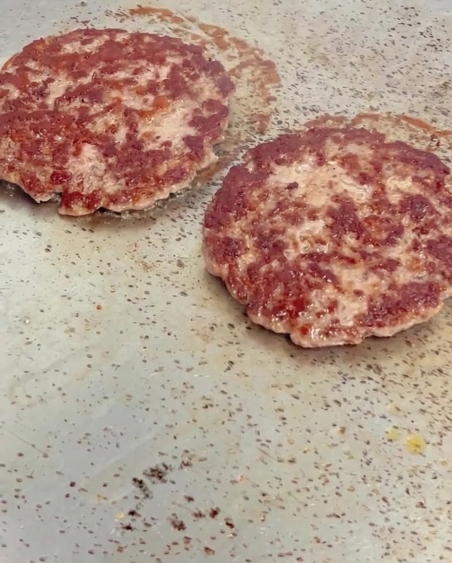 Fette di formaggio giallo che si sciolgono sopra hamburger di manzo caldi e rosolati su una piastra.