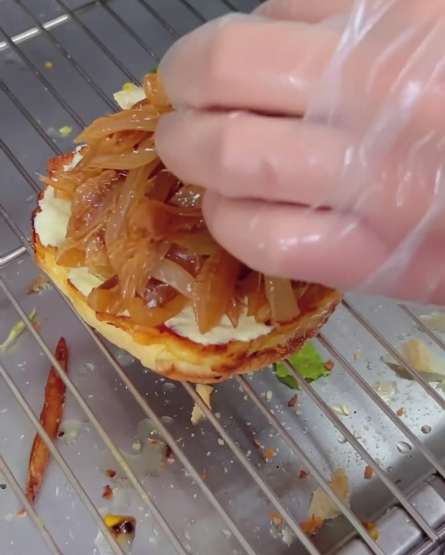 Cipolle caramellate adagiate su un panino con sopra un hamburger al formaggio e il pane a chiudere il tutto.