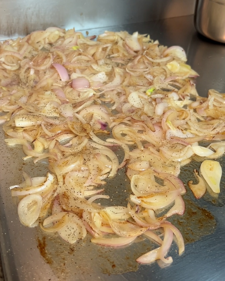 Cipolle in fase di caramellizzazione su una piastra, condite con una spolverata di pepe nero e vivace paprika dolce ungherese.