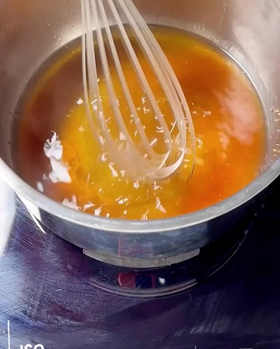 Una frusta mescola confettura di ciliegie, bourbon e zucchero di canna in un pentolino.