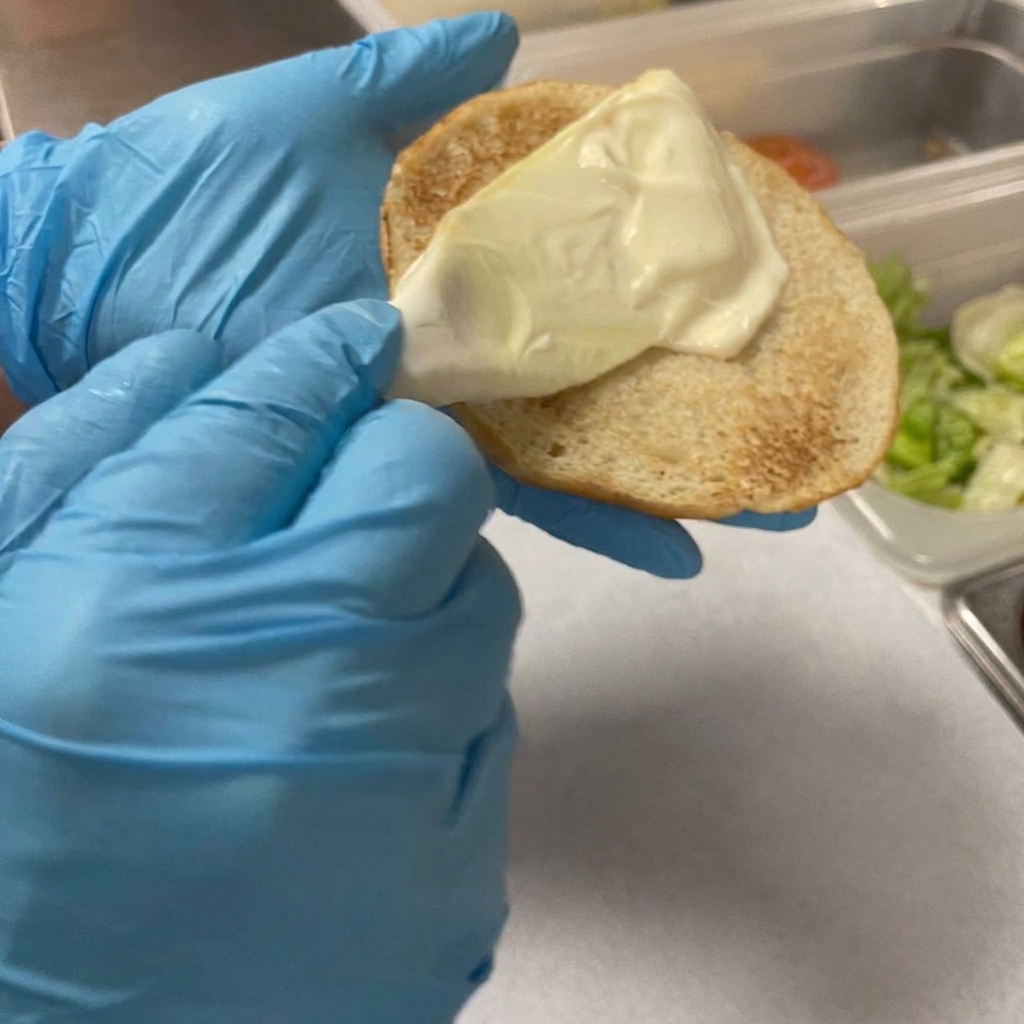Una spatola di plastica che applica uno strato di maionese cremosa sul lato tostato del panino.