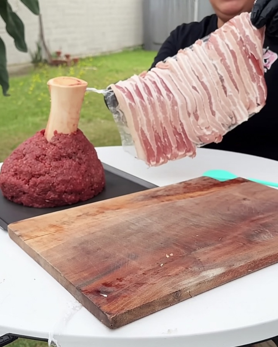 Un blocco quadrato di manzo macinato avvolto accuratamente con strisce di bacon crudo su tutti i lati.