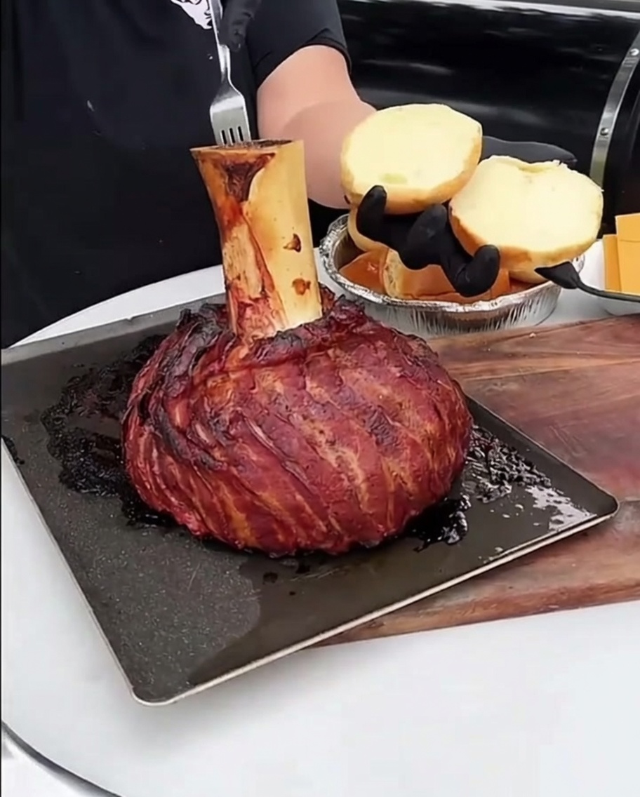Un cucchiaio di ricco midollo osseo arrosto spalmato sulla superficie di un panino per hamburger dorato e tostato.