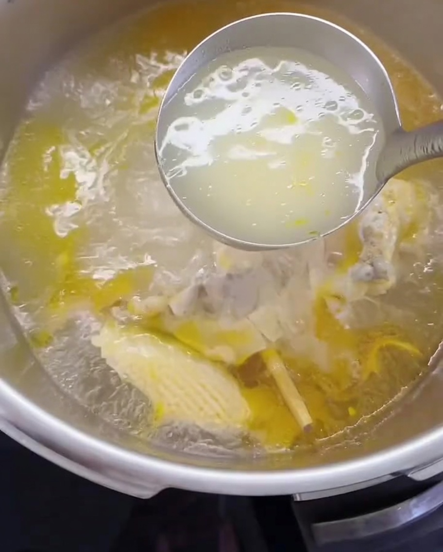 Un mestolo trasferisce il brodo di pollo e la carne sfilacciata in una pentola.