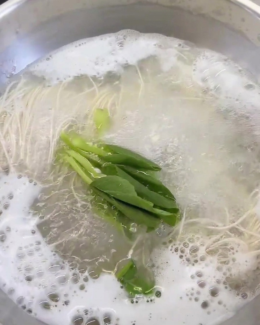 Verdure a foglia verde fresca aggiunte alla pentola con brodo e noodles.
