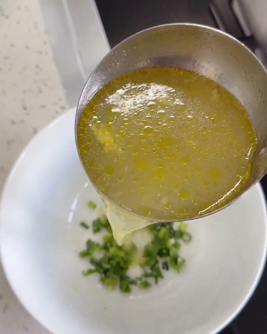 Brodo di pollo caldo versato nella ciotola contenente zenzero e coriandolo.