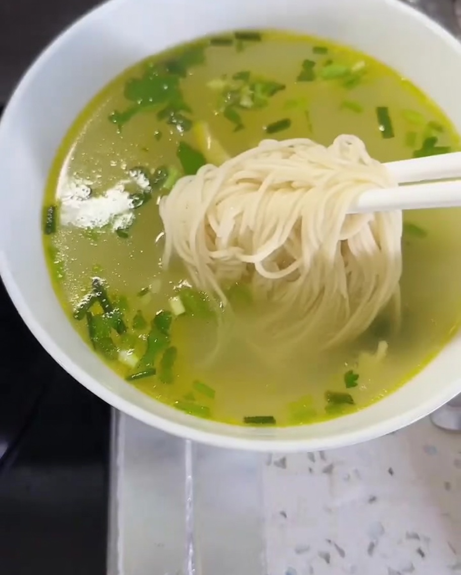 Noodles e verdure trasferiti in una ciotola di brodo per completare il piatto.