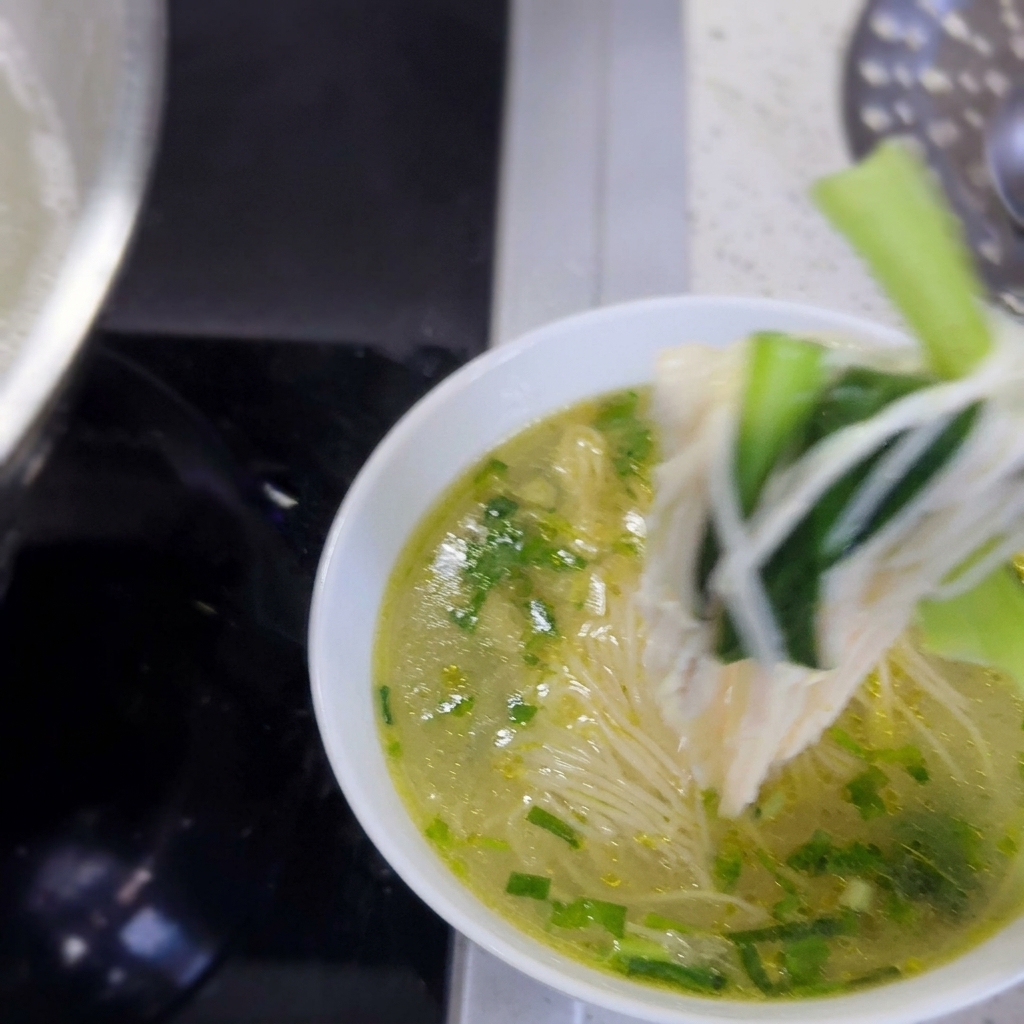 Una ciotola piena di noodles caldi, verdure verdi e tenero pollo sfilacciato pronta per essere servita.