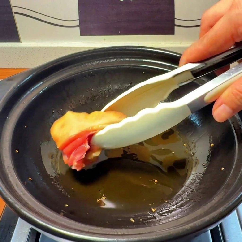 Pezzi di pollo crudo inseriti in una pentola di terracotta con olio caldo infuso allo zenzero.