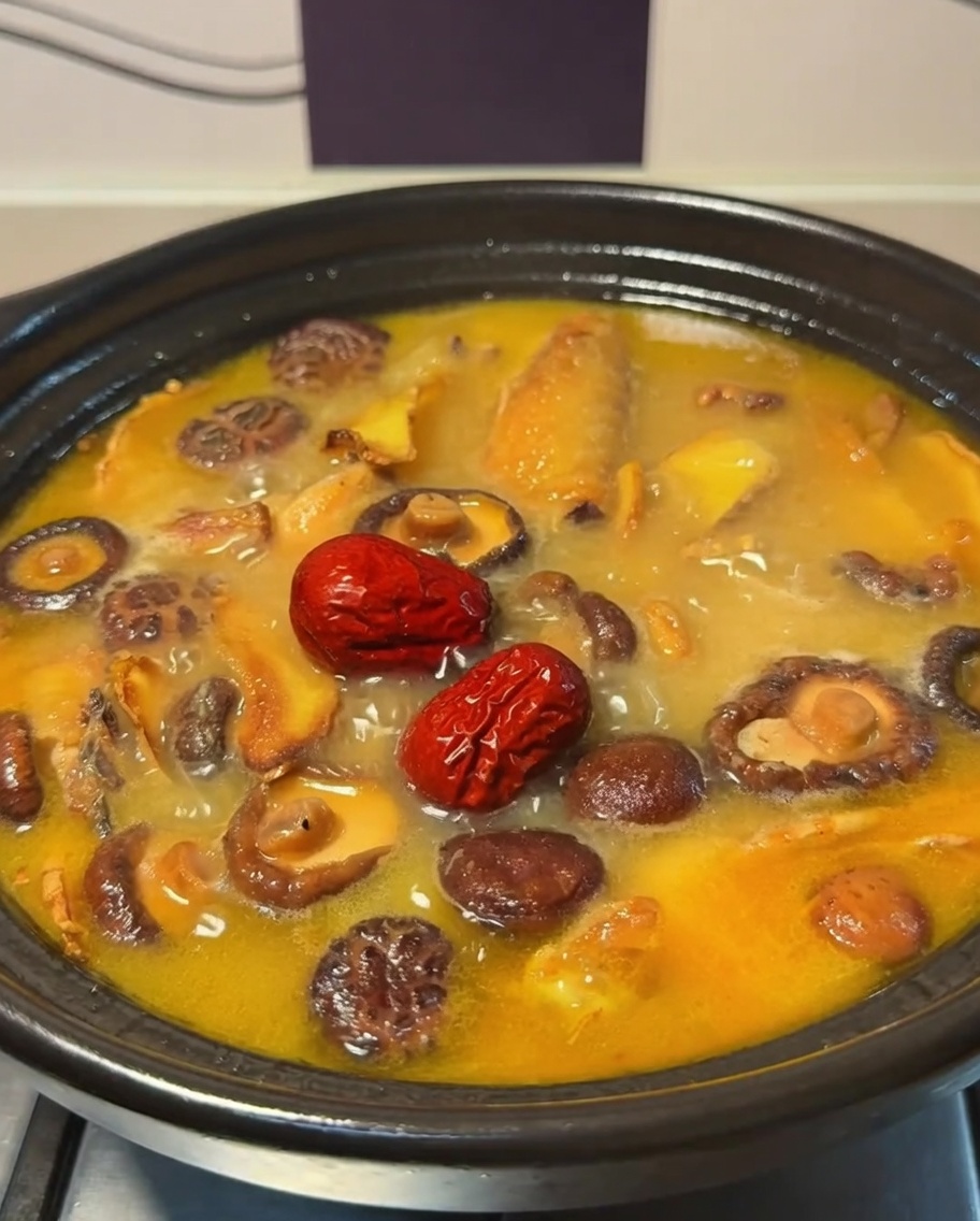 Datteri rossi che galleggiano nel brodo bollente di pollo e funghi allinterno di una pentola in terracotta.