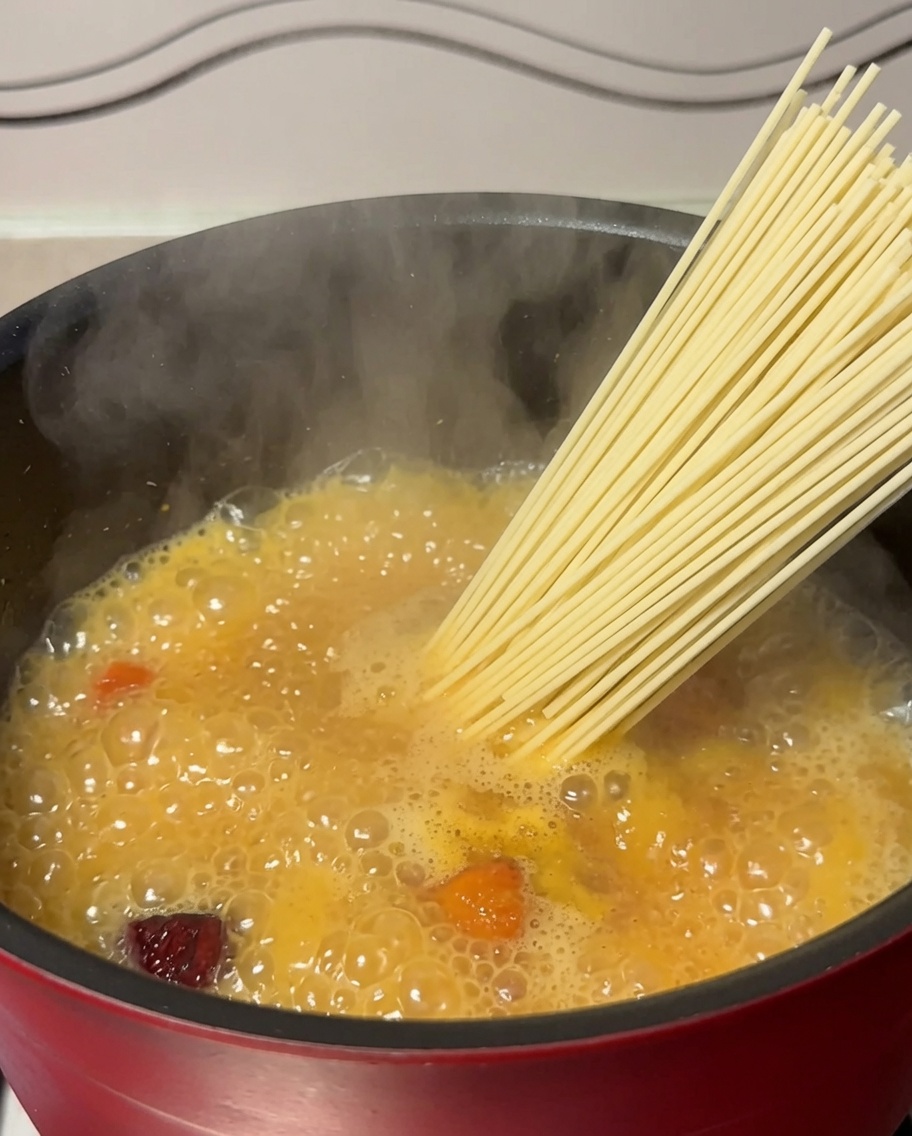 Noodles secchi inseriti in una pentola di zuppa di pollo in ebollizione.