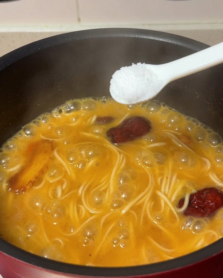 Un cucchiaio di sale aggiunto alla pentola con i noodles in ebollizione e la zuppa di pollo.