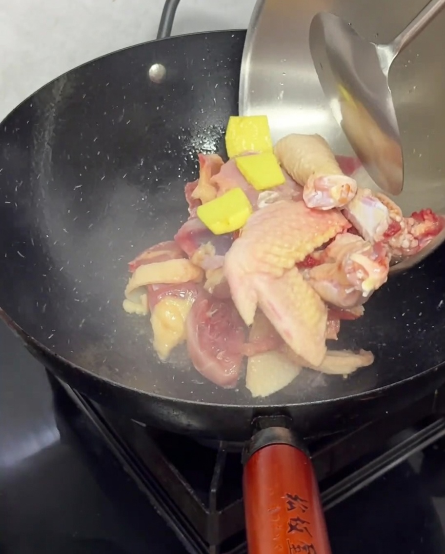 Pezzi di pollo crudo e fette di zenzero messi a soffriggere in un wok caldo.