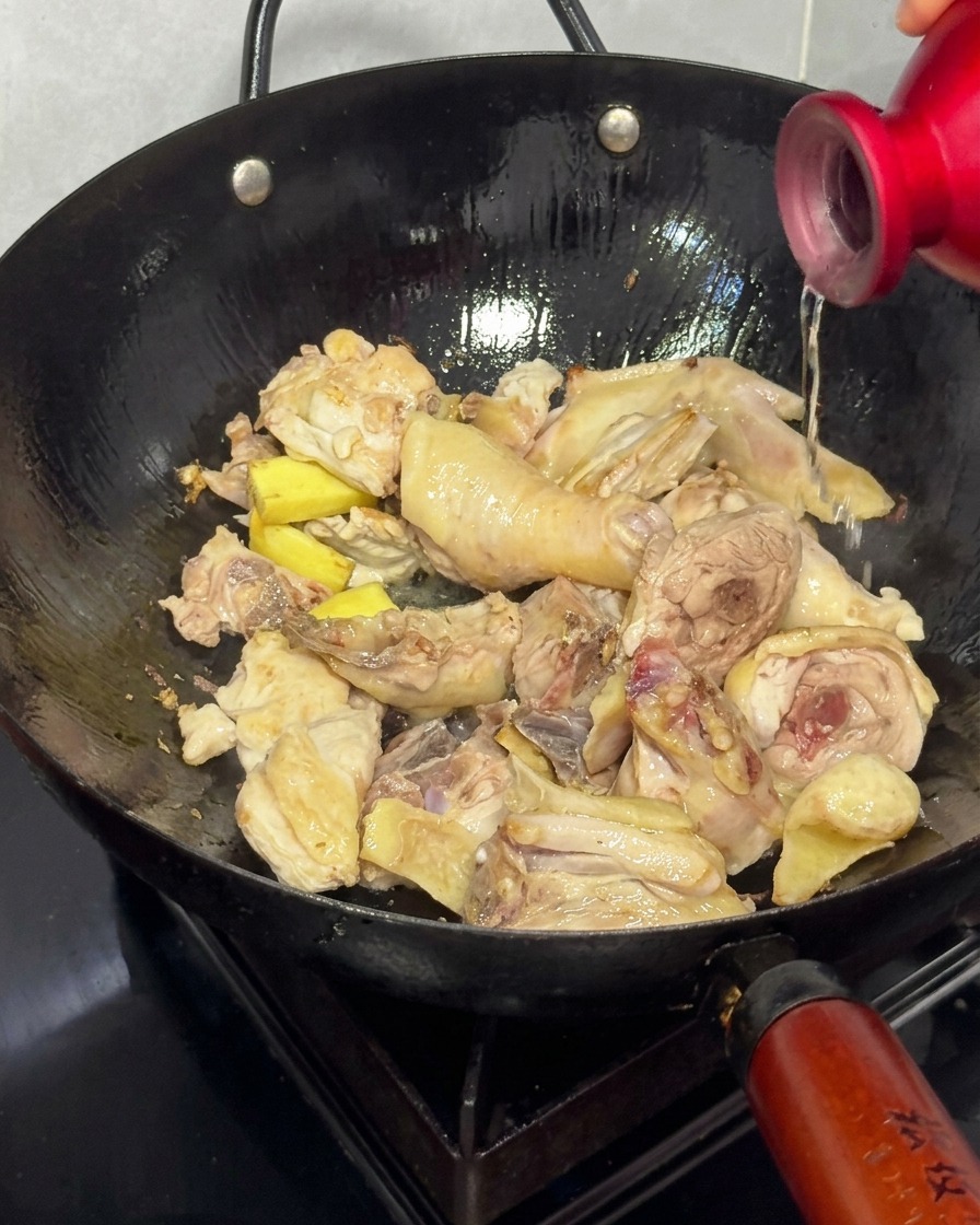 Versare il vino di riso da una bottiglia rossa in un wok con pollo dorato e zenzero.