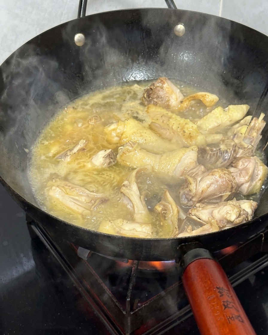 Pezzi di pollo che sobbollono in un wok con un brodo caldo dorato.