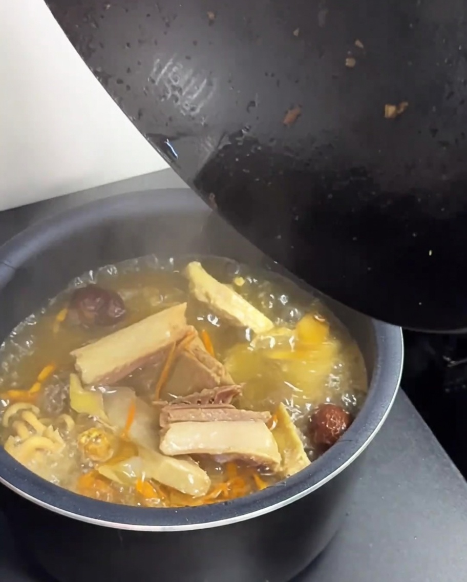 Trasferimento di zuppa di pollo e funghi da un wok a una pentola per cuociriso verde.