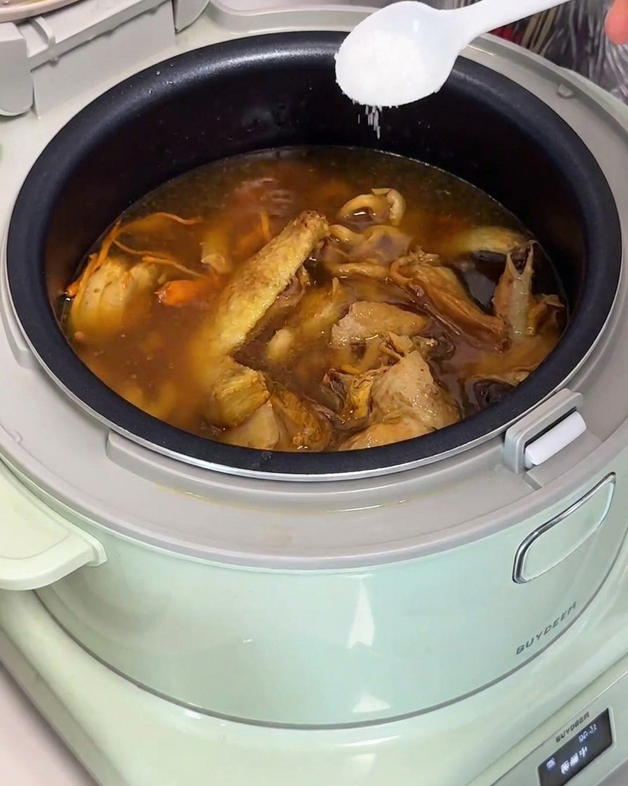 Un cucchiaio bianco che aggiunge sale in una pentola di zuppa di pollo e funghi nella cuociriso.