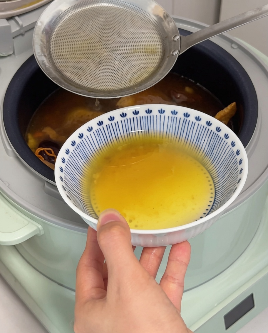 Un primo piano di un mestolo che rimuove uno strato di grasso dorato dalla superficie della zuppa.