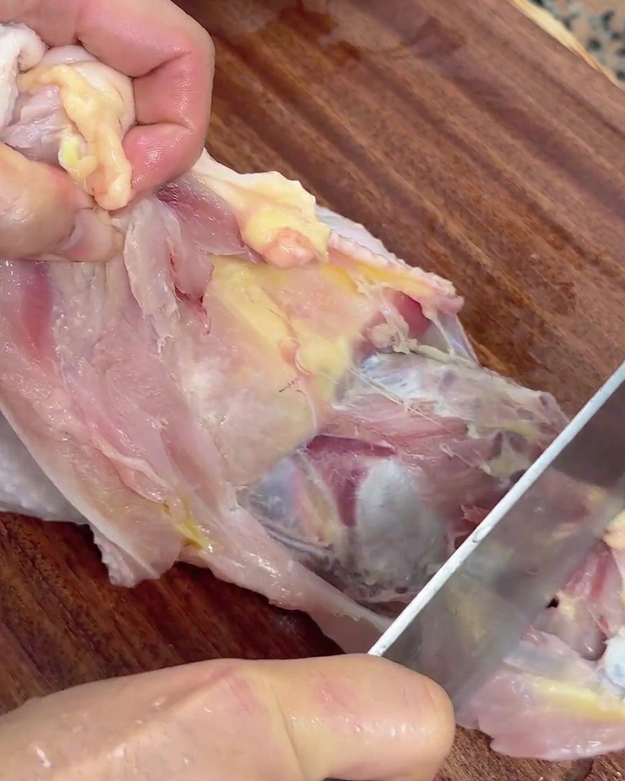 Mani che tengono un pollo crudo e usano un coltello per separare la carne dalla carcassa.