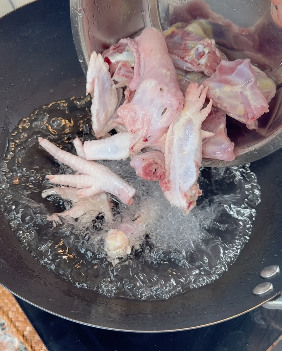 Versare ossa e zampe di pollo crudo in un wok di acqua bollente.