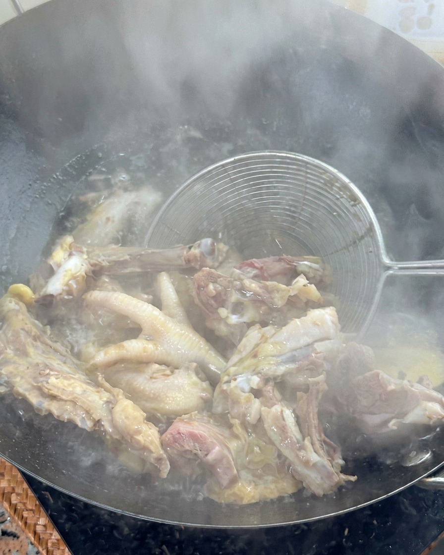Un colino a rete metallica che solleva le ossa di pollo sbollentate da un wok di acqua bollente.