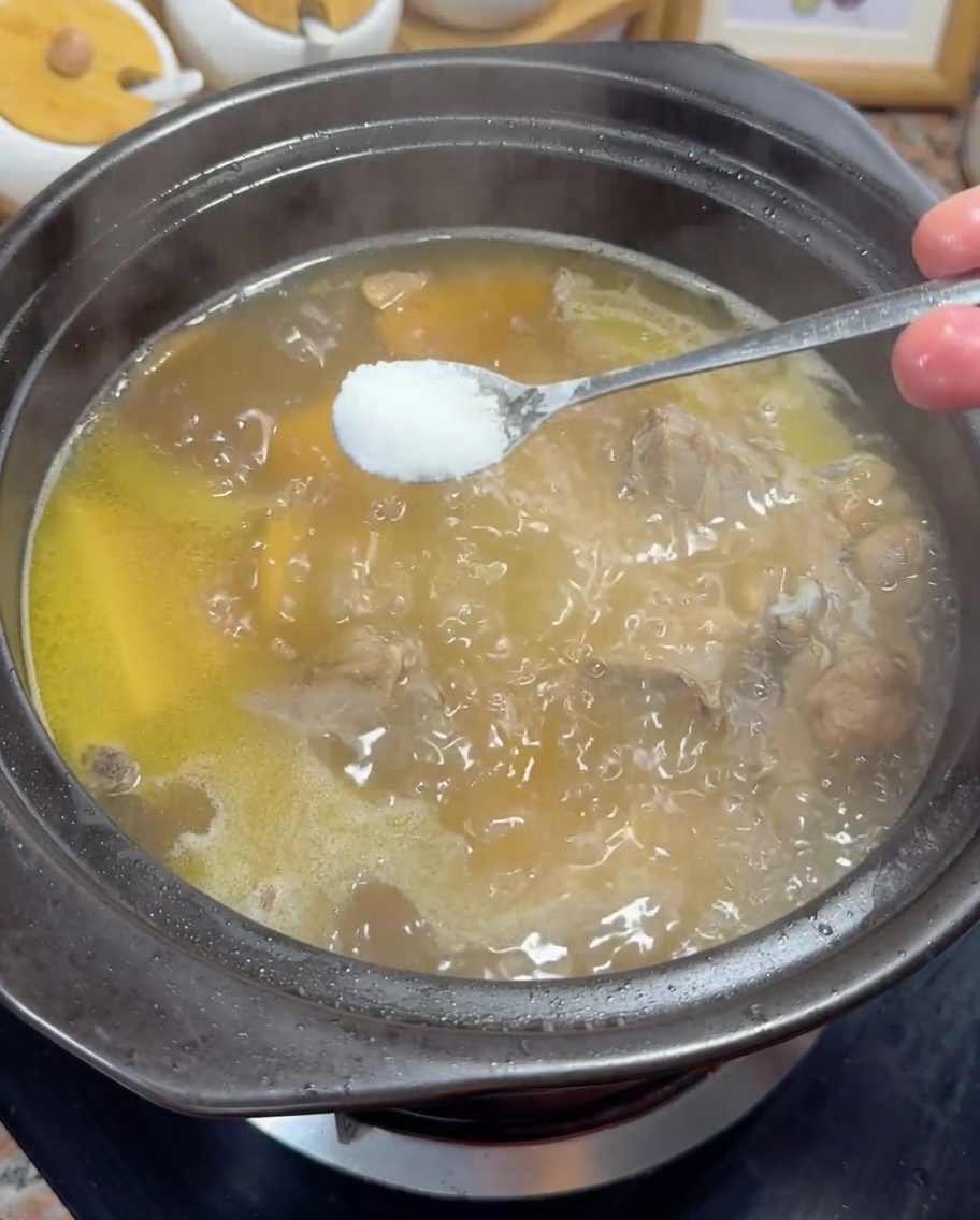 Aggiunta di un cucchiaino di sale bianco in un brodo di pollo dorato che sobbolle.