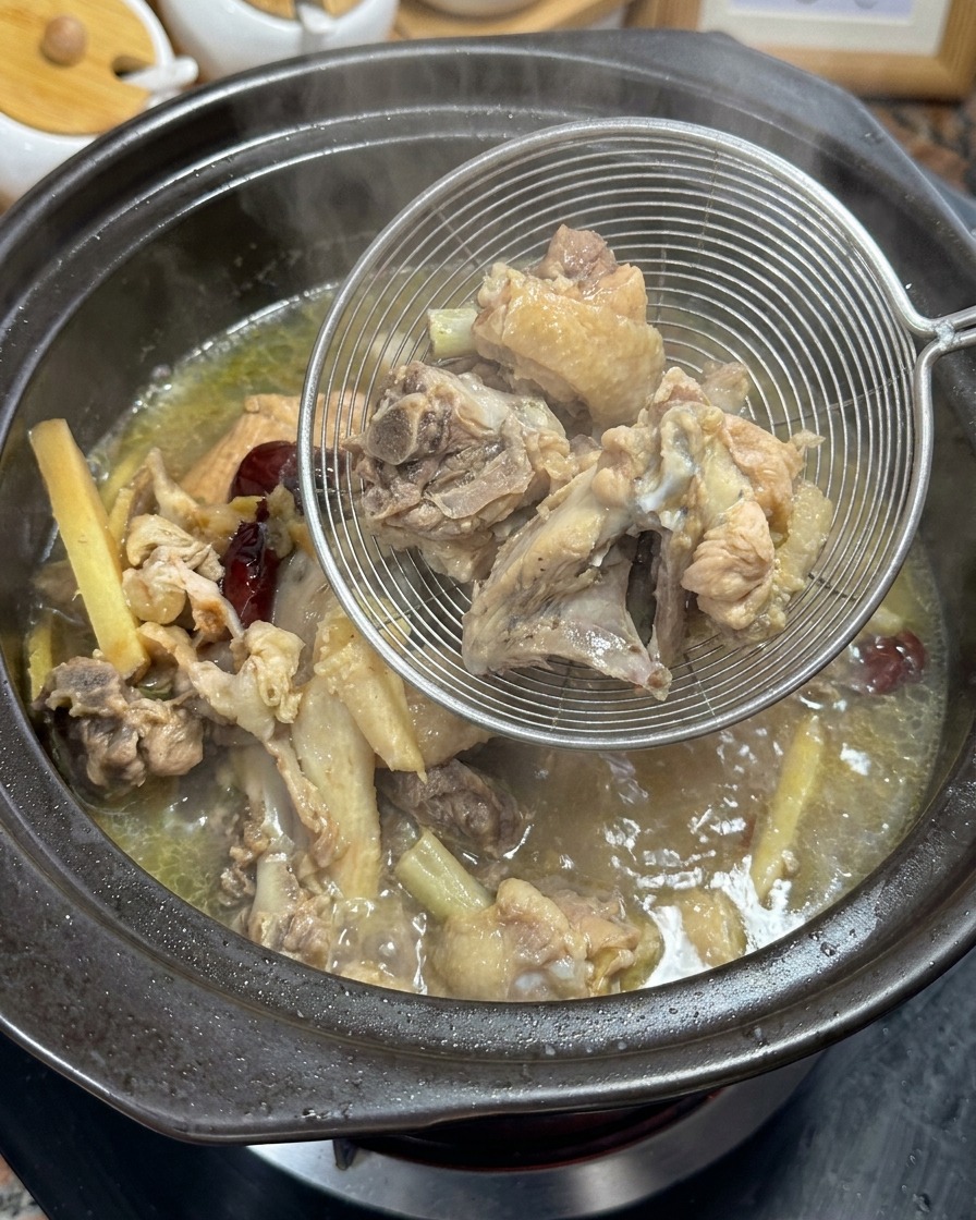 Sollevare ossa di pollo bollite e aromi dal brodo dorato usando un colino metallico.