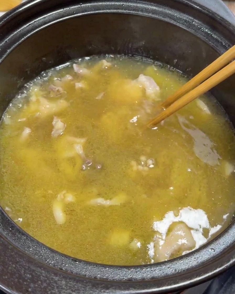 Bacchette che mescolano delicatamente fettine di pollo e tuorli nella zuppa che sobbolle.