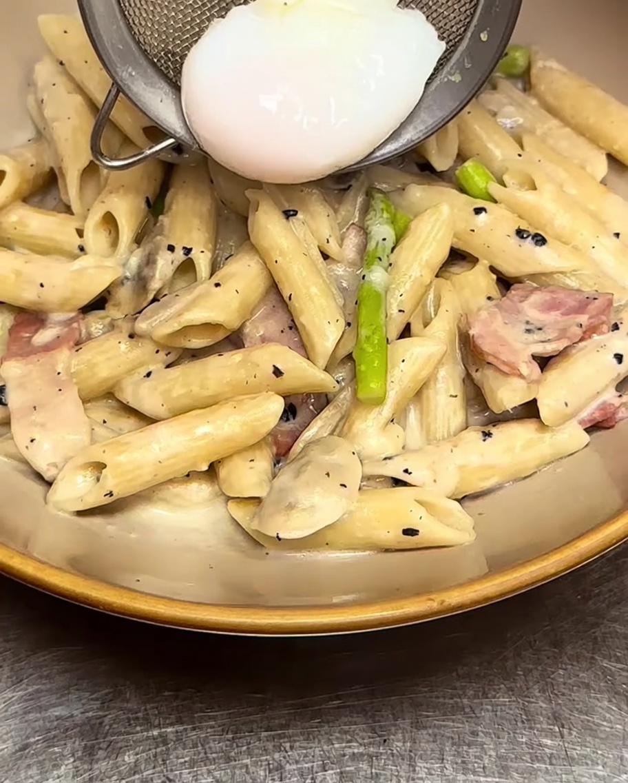 Penne cremose nel piatto con uovo in camicia al centro.